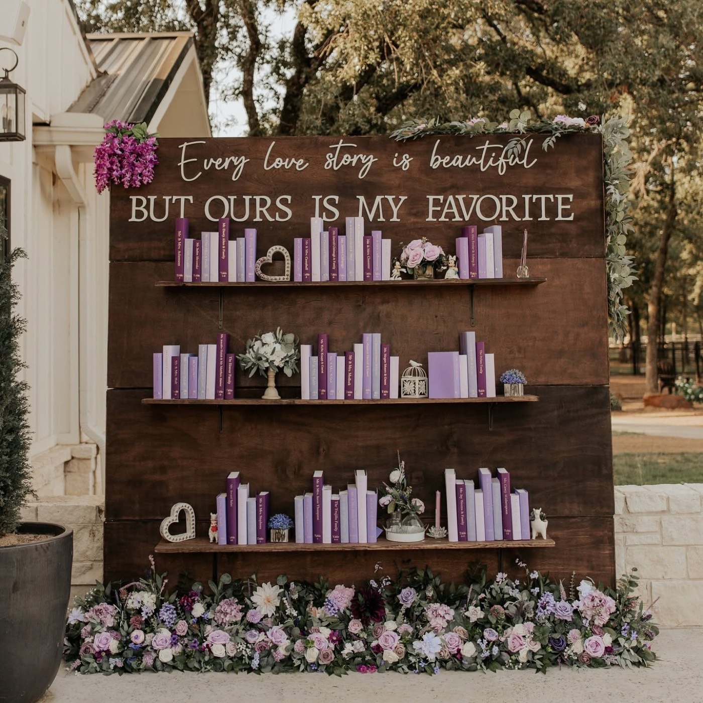 A custom wedding backdrop reading "Every love story is beautiful but ours is my favorite" with lavender books and florals