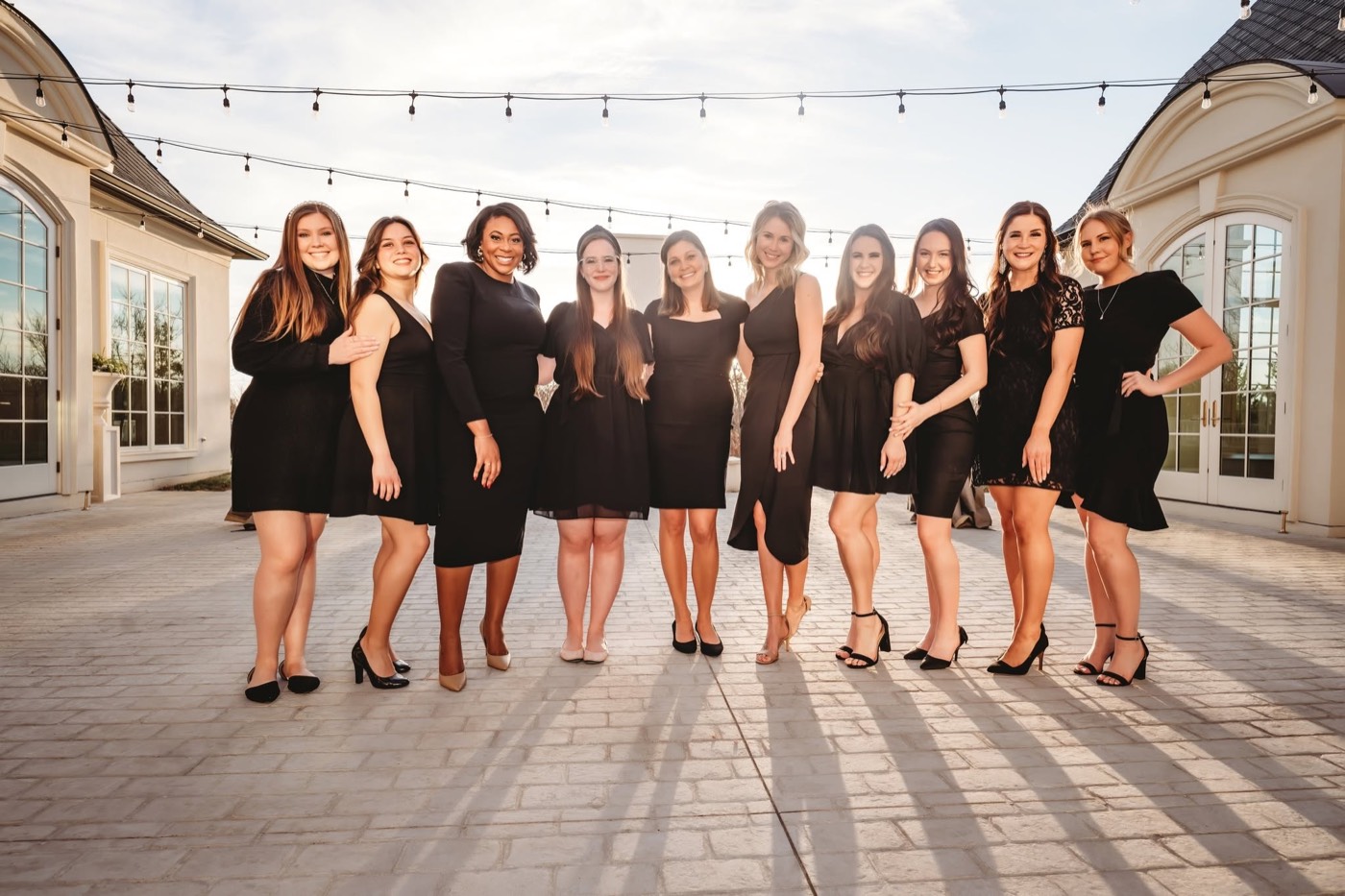 The CM Promotions planning team in black dresses at a Dallas wedding venue under string lights